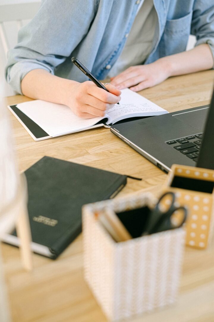 A person writing in a notebook on top of a desk.